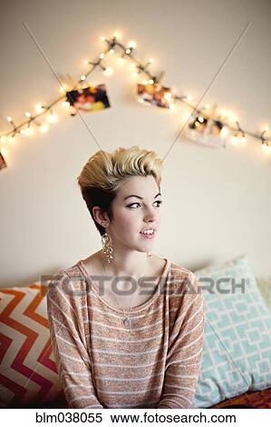 Stock Photography - Woman sitting under string lights in bedroom. Fotosearch