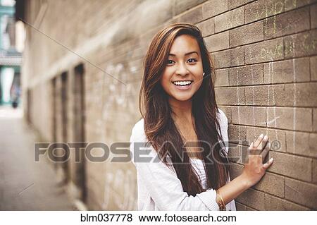 Stock Photo - Woman standing at brick wall in city. Fotosearch