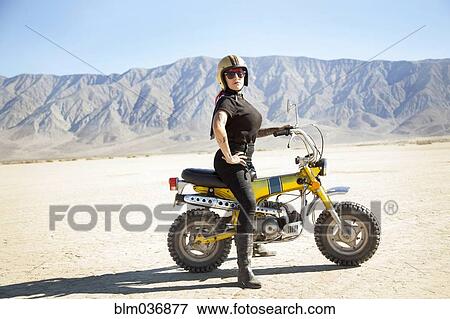 Stock Photo - Woman standing on motorcycle in desert. Fotosearch