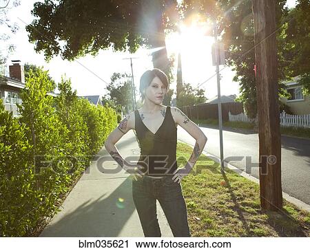 Stock Image - Woman standing on sunny suburban sidewalk. Fotosearch