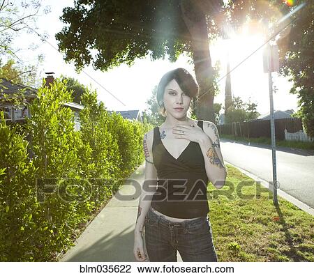 Stock Image - Woman standing on sunny suburban sidewalk. Fotosearch