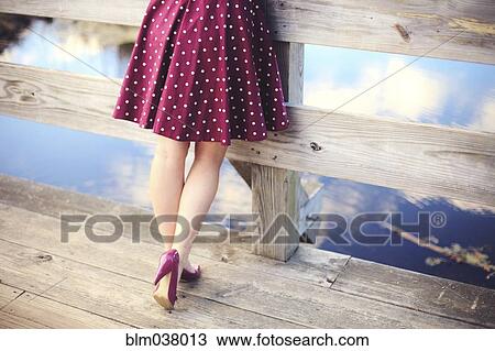 Stock Image - Woman standing on wooden dock over still lake. Fotosearch