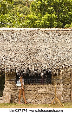 Picture - Woman standing under thatched hut roof. Fotosearch