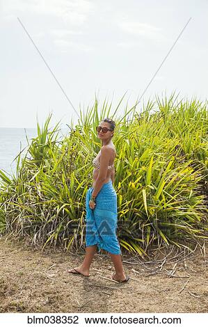 Stock Image - Woman walking near beach grass. Fotosearch