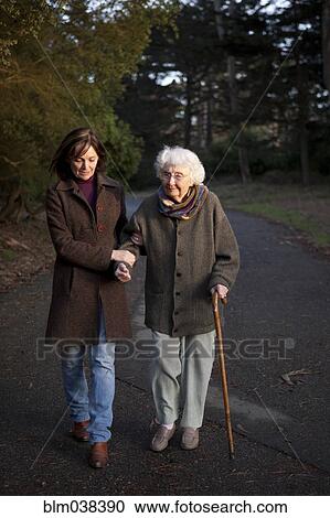 Stock Image - Woman walking with mother on paved path. Fotosearch