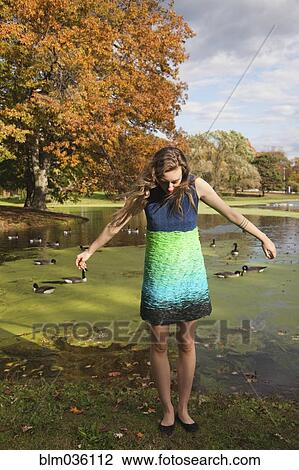 Stock Image - Woman wearing dress near duck pond in park. Fotosearch
