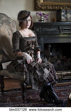Stock Photograph - Woman wearing vintage gown and hat in armchair. Fotosearch