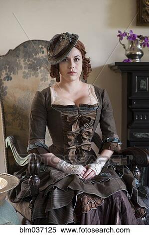 Stock Photography - Woman wearing vintage gown and hat in armchair. Fotosearch
