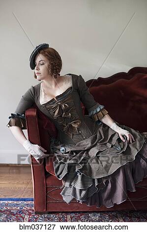 Woman wearing vintage gown and hat on sofa View Large Photo Image Stock Photo - Woman wearing vintage gown and hat on sofa. Fotosearch