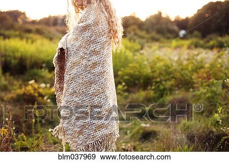 Stock Photo - Woman wrapped in blanket walking in field. Fotosearch