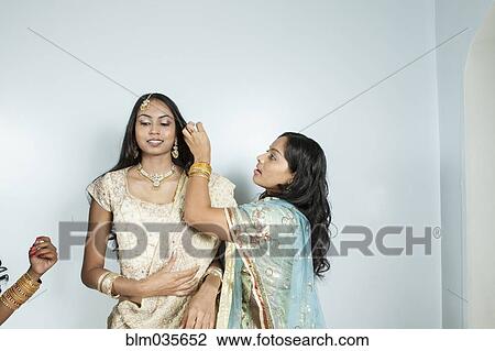Stock Image - Women dressing bride in traditional dresses and jewelry. Fotosearch