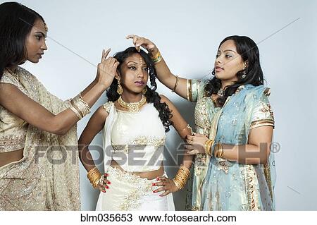 Stock Image - Women dressing bride in traditional dresses and jewelry. Fotosearch