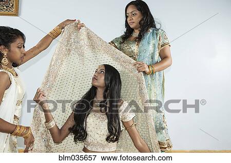 Stock Photo - Women dressing bride in traditional dresses and jewelry. Fotosearch