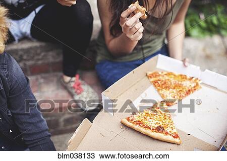 Stock Image - Women eating pizza on front steps. Fotosearch