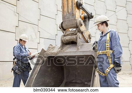 Picture - Workers examining digger machinery at construction site. Fotosearch