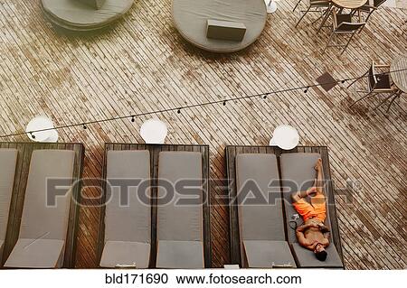 Stock Image - Aerial view of man laying on deck chair. Fotosearch
