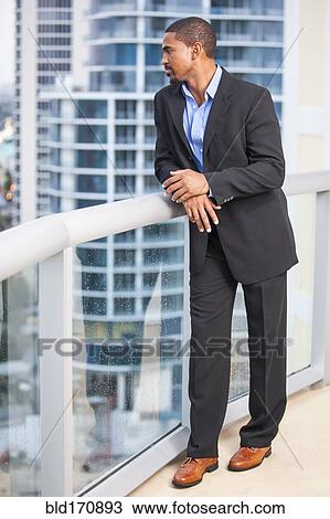 Stock Image - African American businessman standing on urban balcony. Fotosearch