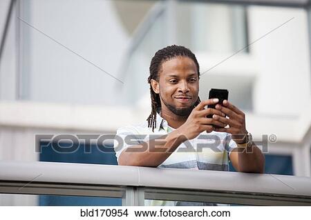 Picture - African American businessman using cell phone on balcony. Fotosearch