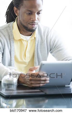 Stock Photo - African American businessman using digital tablet in restaurant. Fotosearch