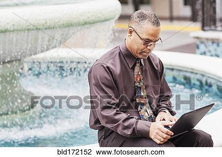 Stock Image - African American businessman working at fountain. Fotosearch