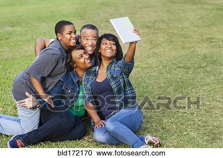 Stock Image - African American family taking selfie with digital tablet on grass. Fotosearch