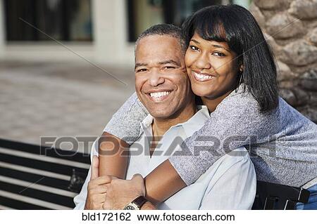 Stock Image - African American father and daughter hugging on bench. Fotosearch