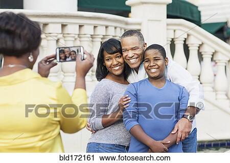 Stock Image - African American woman taking cell phone photograph of family. Fotosearch