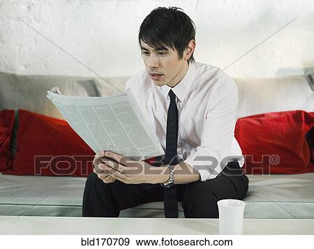 Stock Photo - Asian businessman reading newspaper on sofa. Fotosearch