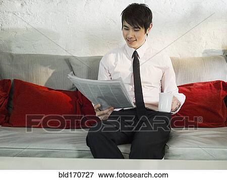 Stock Photo - Asian businessman reading newspaper on sofa. Fotosearch