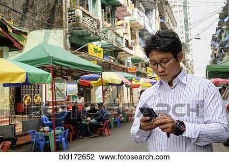 Stock Image - Asian businessman using cell phone in city. Fotosearch