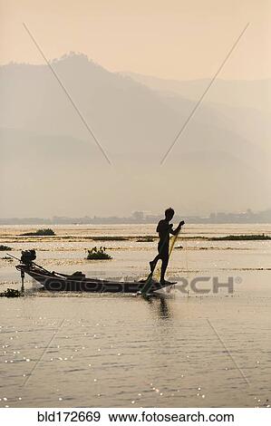 Asian fisherman rowing canoe on rural lake View Large Photo Image Stock Photo - Asian fisherman rowing canoe on rural lake. Fotosearch