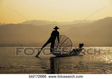 Stock Photograph - Asian fisherman rowing canoe on rural lake. Fotosearch
