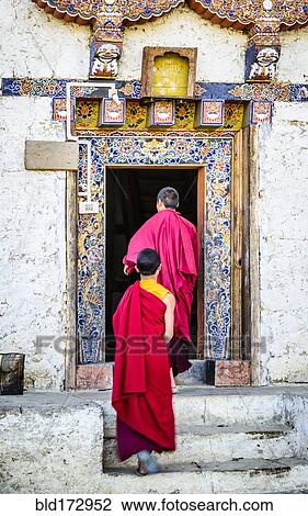 Stock Image - Asian monks walking in temple doorway. Fotosearch