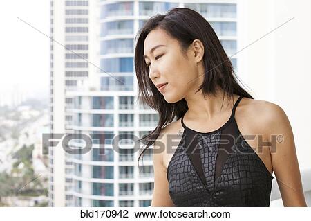 Stock Image - Asian woman on urban balcony. Fotosearch