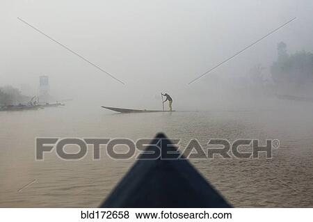 Stock Photo - Asian woman rowing canoe on rural lake. Fotosearch