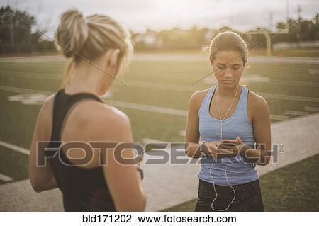 Stock Image - Athletes listening to mp3 players on sports field. Fotosearch