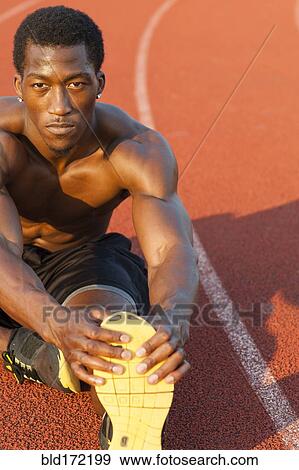 Stock Photo - Black athlete stretching on track in sports field. Fotosearch