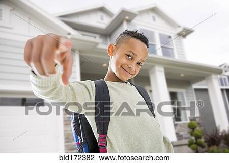 Stock Image - Black boy in backpack pointing on front lawn. Fotosearch