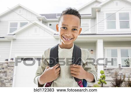 Stock Image - Black boy in backpack smiling outside house. Fotosearch