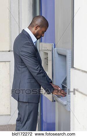 Stock Image - Black businessman using ATM in city. Fotosearch