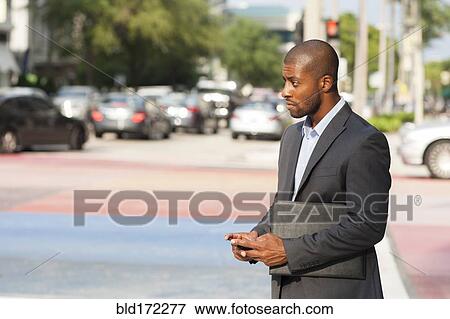 Stock Photo - Black businessman using cell phone at crosswalk. Fotosearch