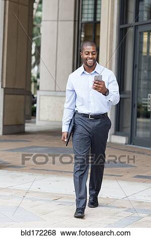 Stock Photo - Black businessman using cell phone on city sidewalk. Fotosearch