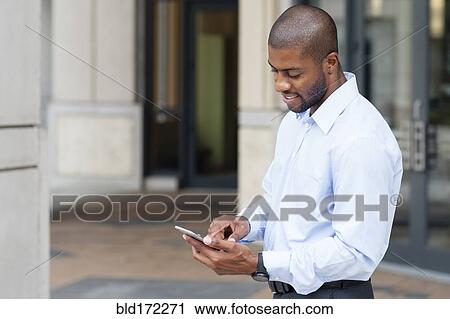 Stock Image - Black businessman using cell phone outside office. Fotosearch