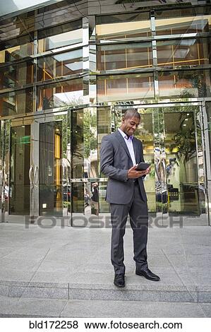 Stock Photo - Black businessman using digital tablet outside office building. Fotosearch