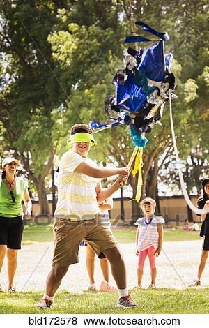 Stock Photo - Blindfolded boy hitting pinata at party. Fotosearch