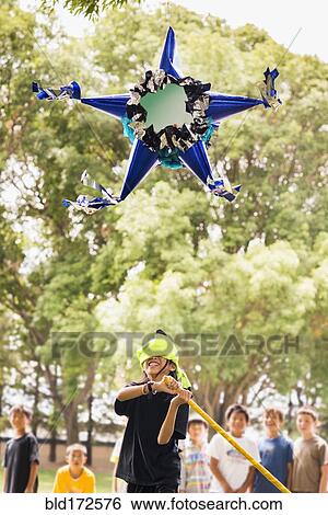 Stock Photograph - Blindfolded boy hitting pinata at party. Fotosearch