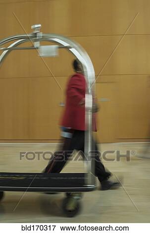 Stock Photo - Blurred view of bellhop and luggage cart in hotel. Fotosearch