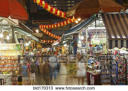 Stock Image - Blurred view of people shopping in outdoor market at night. Fotosearch