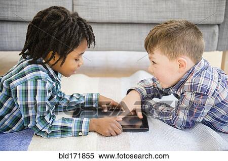 Stock Photography - Boys playing with digital tablet on sofa. Fotosearch