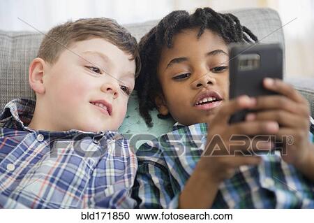 Stock Image - Boys using cell phone on sofa. Fotosearch